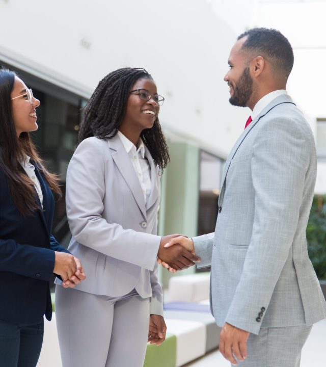 Happy joyful diverse business partners greeting each other Happy joyful diverse business partners greeting each other in hallway. Business man and women standing, shaking hands with each other, talking and smiling. Successful partnership concept
